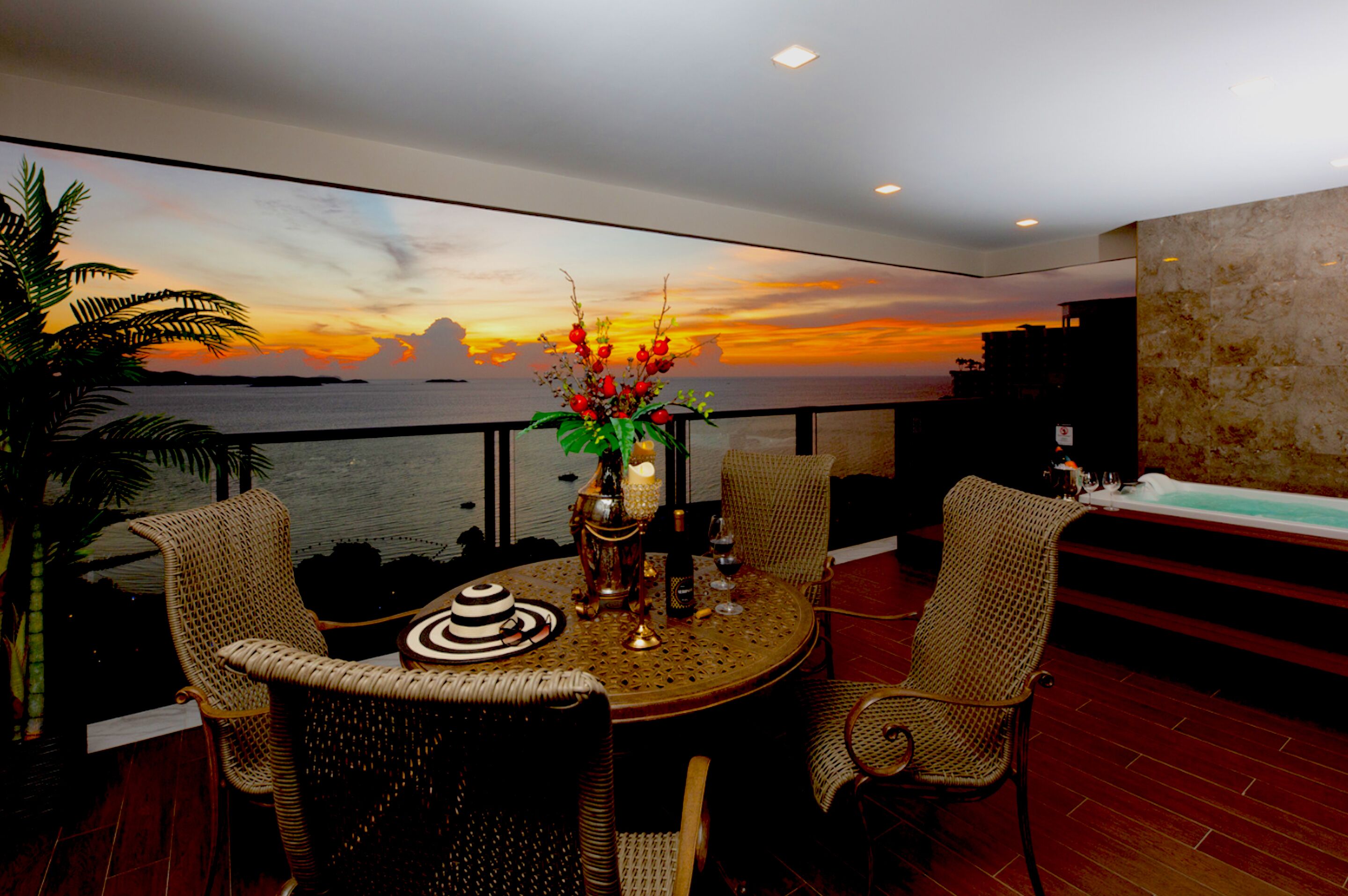 A dining area with a round table, wicker chairs, and a view of the sunset over the ocean.