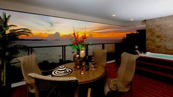 A dining area with a round table, wicker chairs, and a view of the sunset over the ocean.