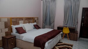 Um quarto com cama, mesas de cabeceira, escrivaninha e cortinas.