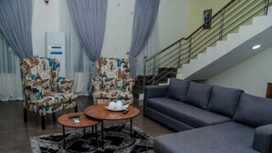 Sala de estar com duas poltronas estampadas, um sofá azul e uma mesa redonda pequena com um controle remoto.