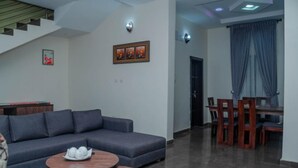 Uma sala de estar com sofá, duas mesinhas de centro, um espaço de jantar com mesa e cadeiras e uma escada.