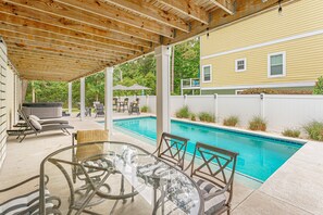 Un espacio al aire libre techado con piscina, sillas de descanso y una mesa.