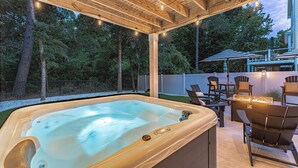 A hot tub under a wooden pergola with string lights, surrounded by outdoor furniture and a view of trees. - 34 Luxury Beach House w/ Pool & Hot Tub | FirePit | Fenced Yard | Sleeps 24 (Hilton Head Island)