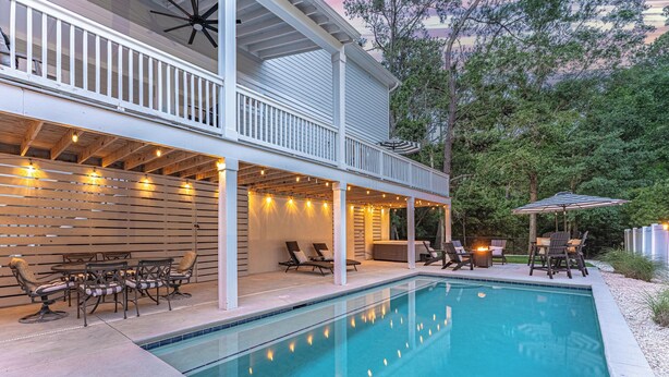 A poolside area with a covered deck, outdoor furniture, and string lights. - 34 Luxury Beach House w/ Pool & Hot Tub | FirePit | Fenced Yard | Sleeps 24 (Hilton Head Island)