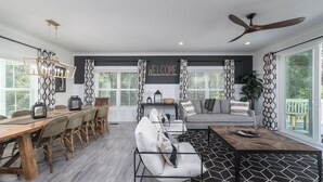 A modern living room with a dining area, a sofa, a coffee table, and a ceiling fan. - 34 Luxury Beach House w/ Pool & Hot Tub | FirePit | Fenced Yard | Sleeps 24 (Hilton Head Island)