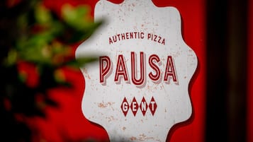 Un letrero con el texto 'Authentic Pizza Pausa' sobre un fondo rojo.