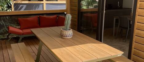 An outdoor wooden deck with a picnic table and benches, a cactus plant, and a view of the interior through an open door.