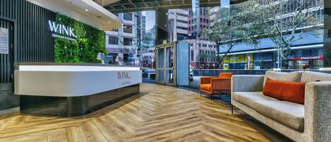 A reception area with a modern design, featuring a wooden herringbone floor, a reception desk, and a seating area with a sofa and chairs.