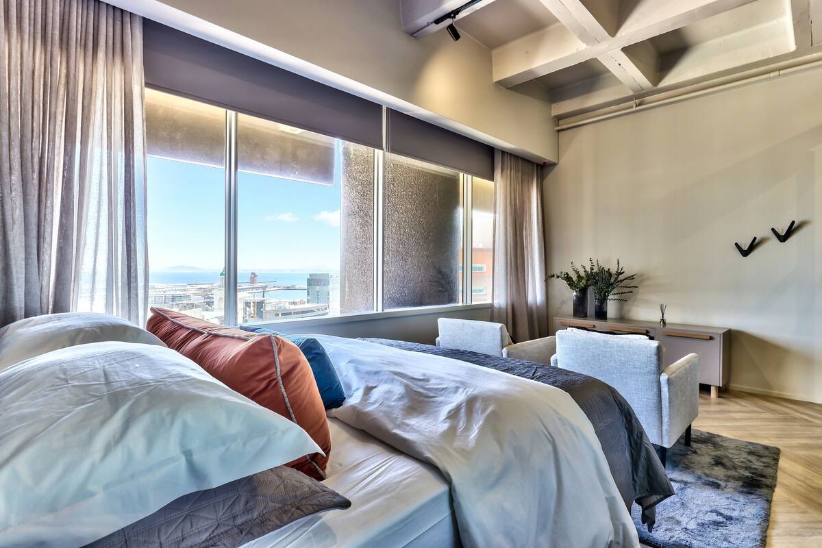 A modern hotel room with a large bed, a desk, and a view of the cityscape.