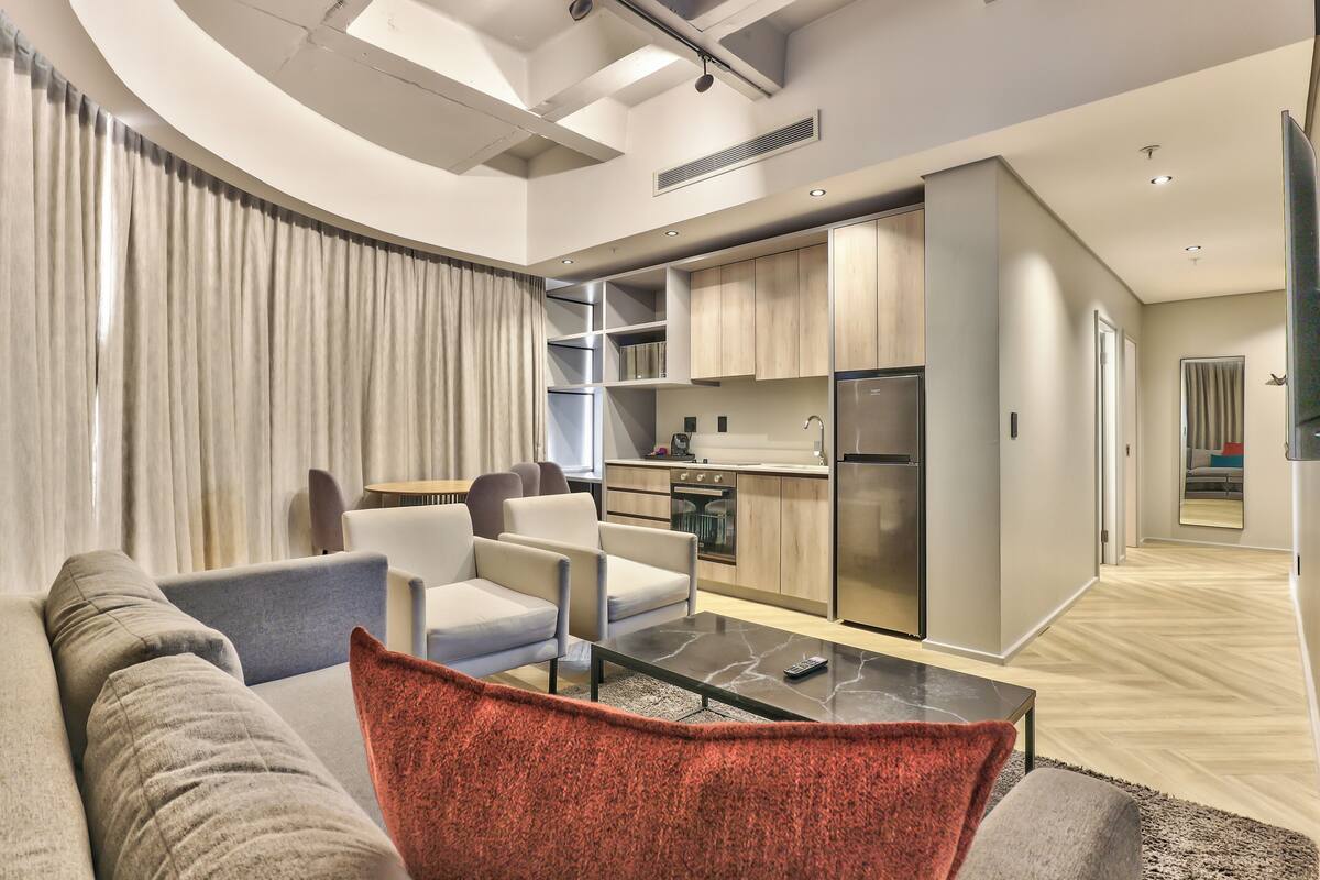 A modern living room with a sofa, a coffee table, and a kitchen area with cabinets and appliances.