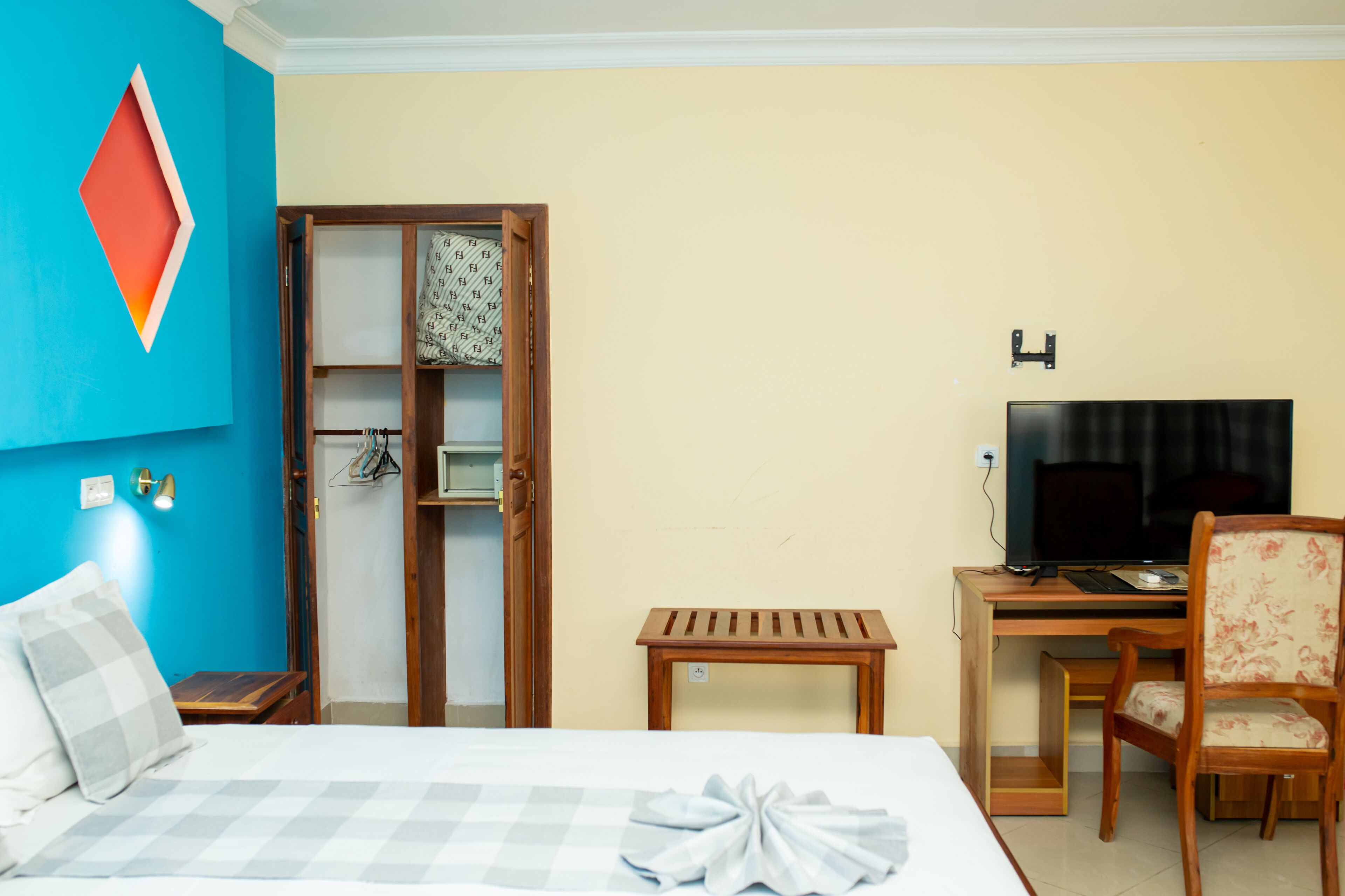 A hotel room with a bed, a desk with a computer and TV, a wooden chair, and a wardrobe.