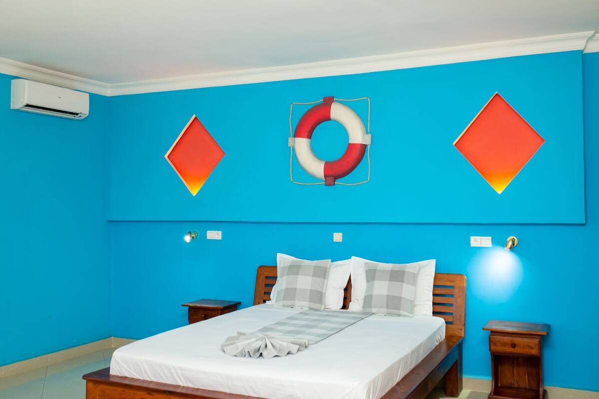 A room with a bed, a wall-mounted air conditioner, and a life preserver decoration.