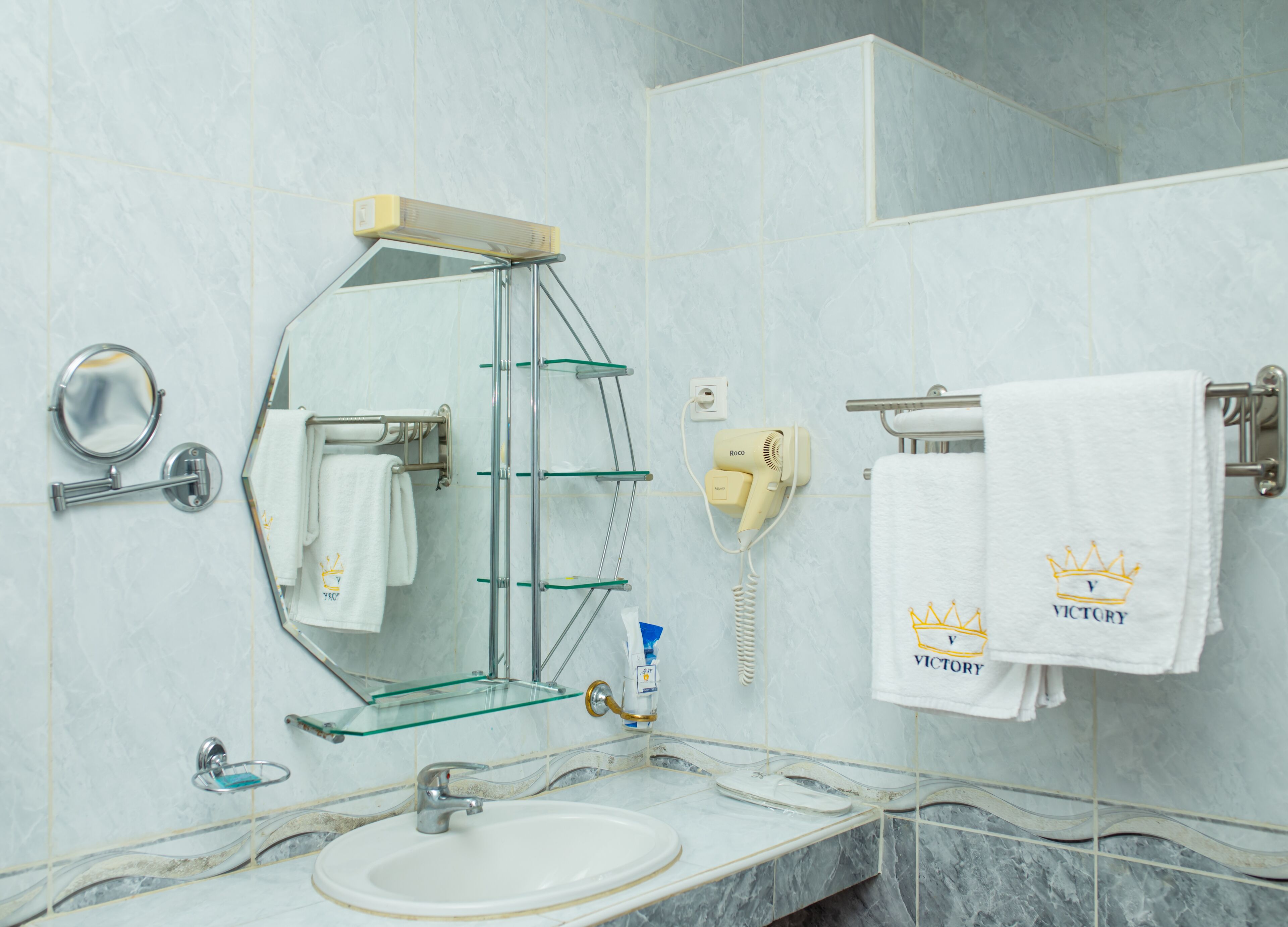 A bathroom with a glass shower enclosure, a sink, a mirror, and a hairdryer mounted on the wall.