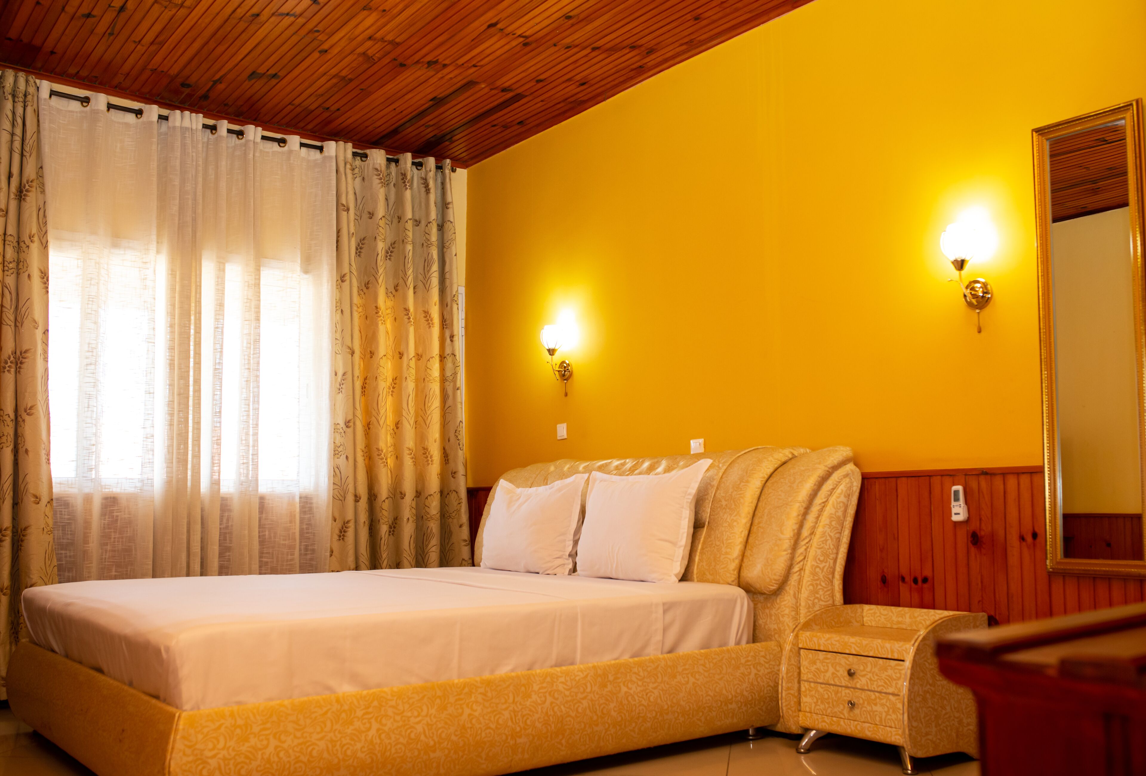 A bedroom with a bed, a nightstand, a mirror, and two wall-mounted lights.