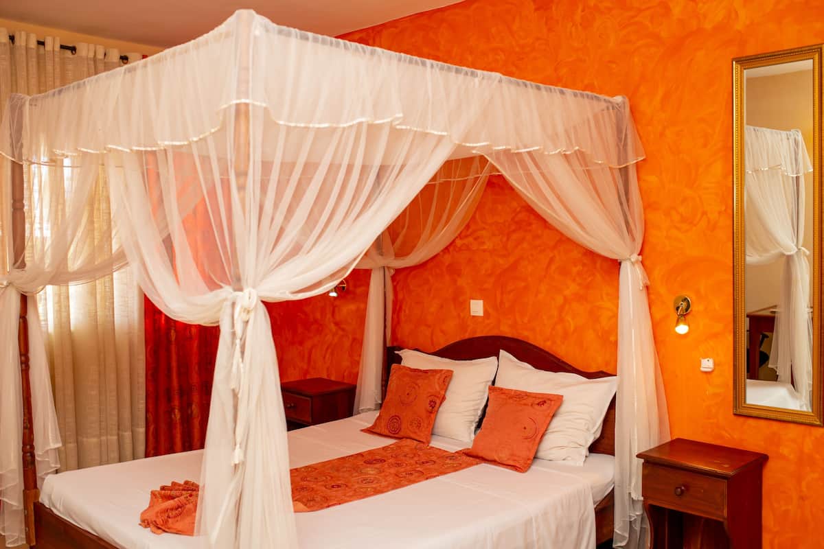 A four-poster canopy bed with white bedding, a red throw, and two pillows.