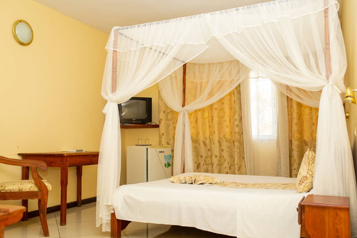 A room with a bed under a canopy, a desk with a chair, a television, and a refrigerator.