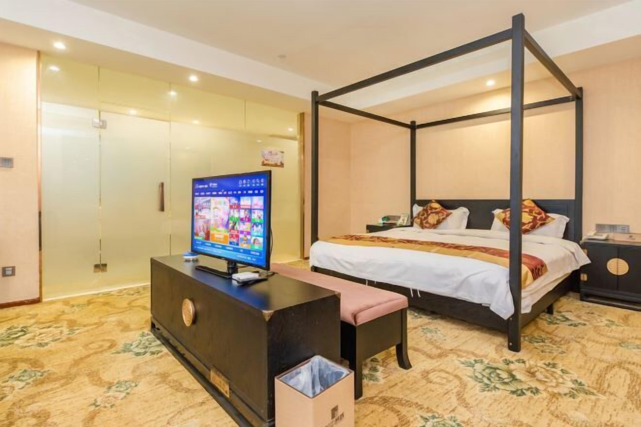 Ein Hotelzimmer mit einem Himmelsbett, einem Fernseher auf einem Standfuß, einer Bank und einem Mülleimer.