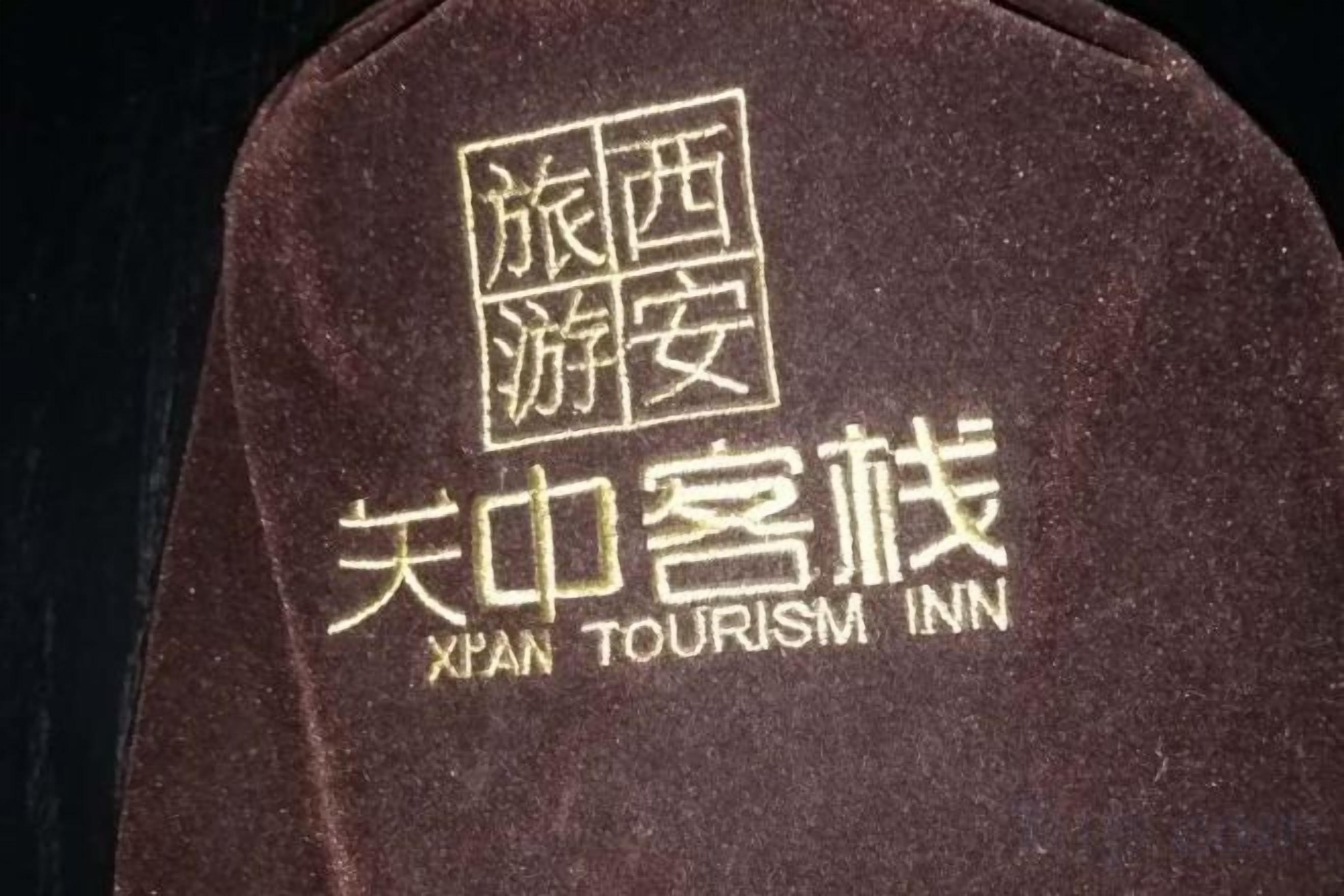 A dark brown fabric with embroidered text in Chinese and English, reading 'Xian Tourism Inn.'