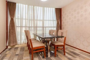 Sala de conferências com mesa de vidro, cadeiras bege, carpete estampado e grandes janelas com cortinas translúcidas.