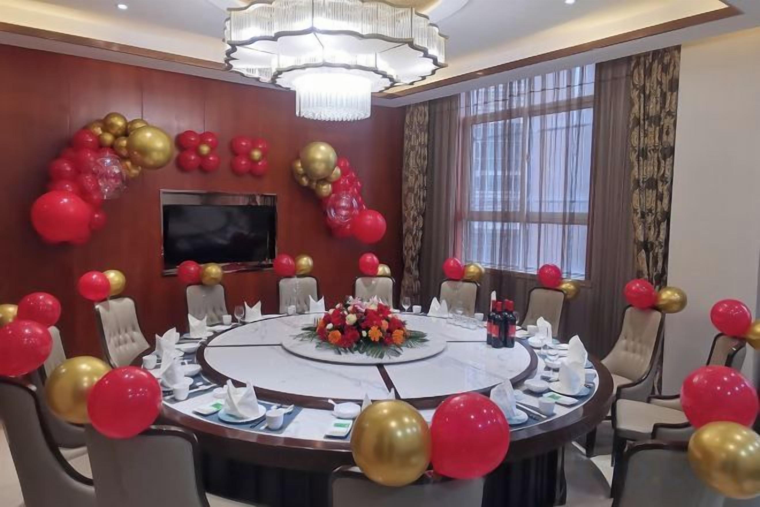 A conference room with a round table, chairs, a television, and red and gold balloons.
