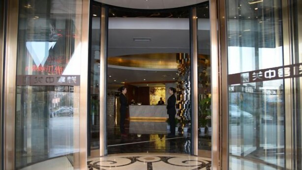 Entrada de un hotel con mostrador de recepción, puertas de vidrio y suelo de mármol.