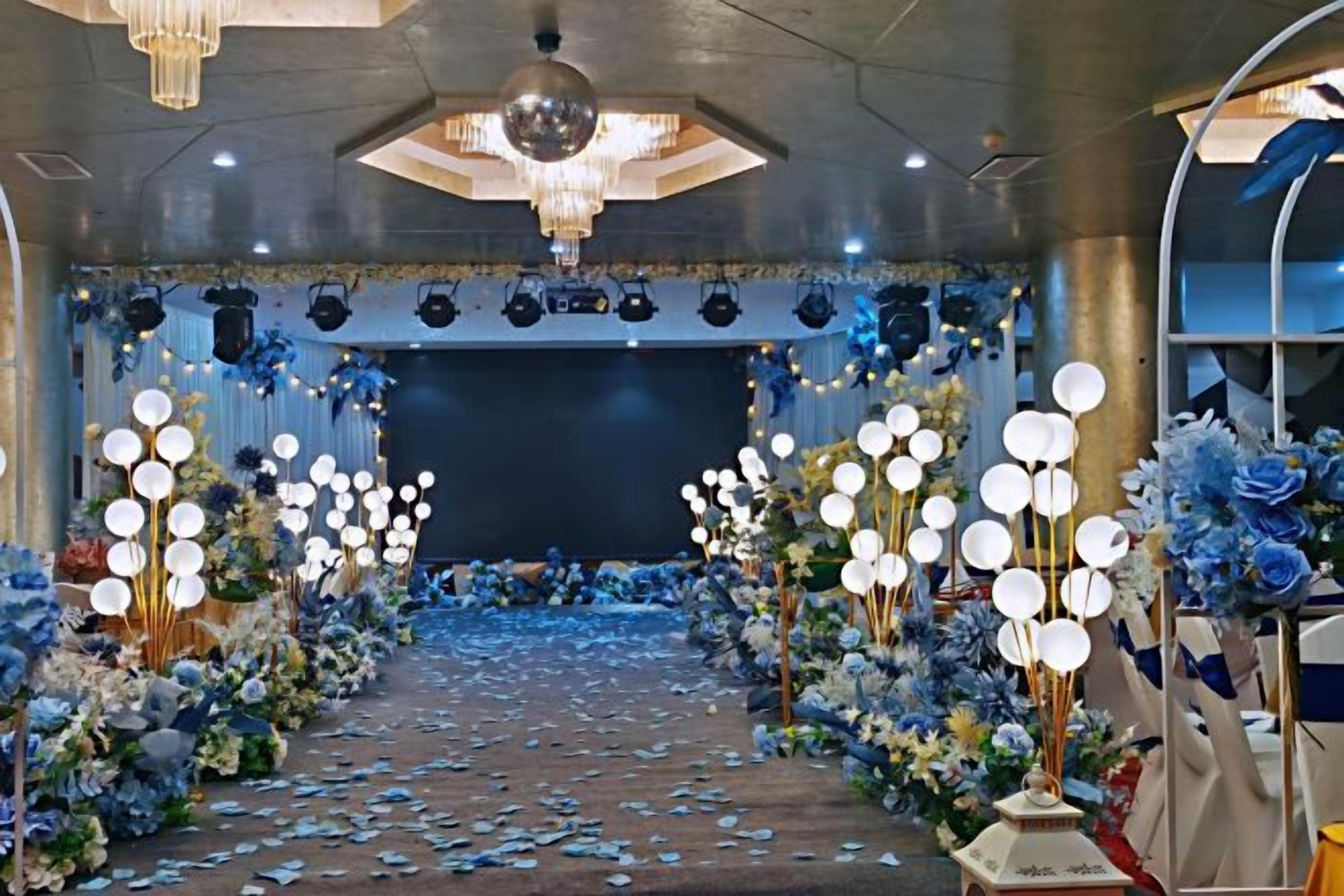 Un espacio interior con escenario, arreglos florales y una araña.