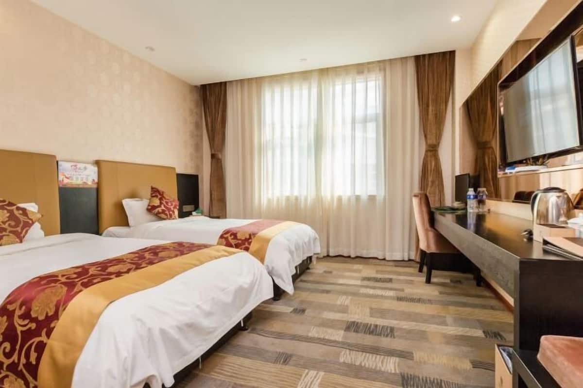 Ein Hotelzimmer mit zwei Betten, einem Schreibtisch, einem Fernseher und einem großen Fenster mit Vorhängen.