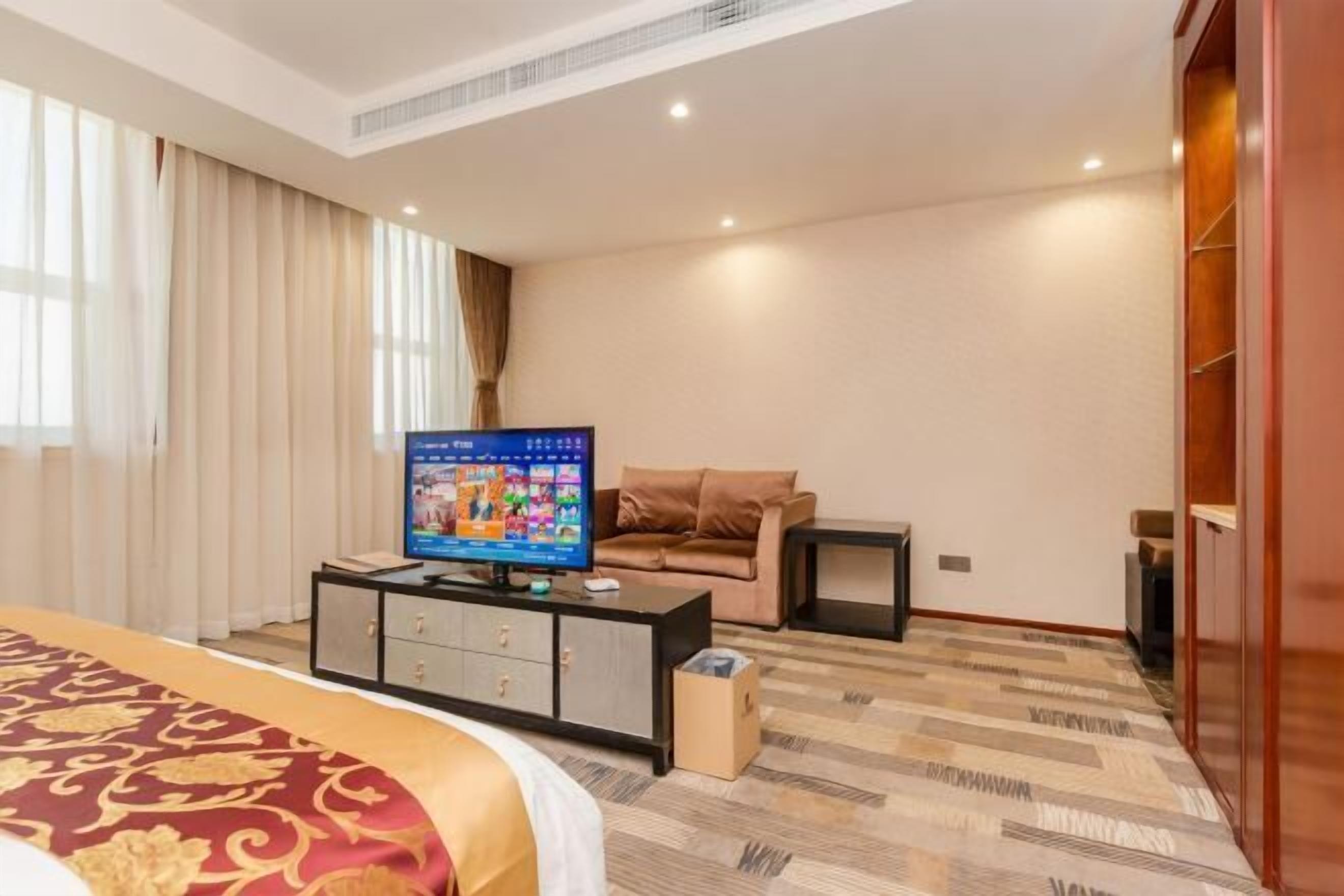 Una habitación de hotel con cama, televisor, sofá, una mesita y un armario.