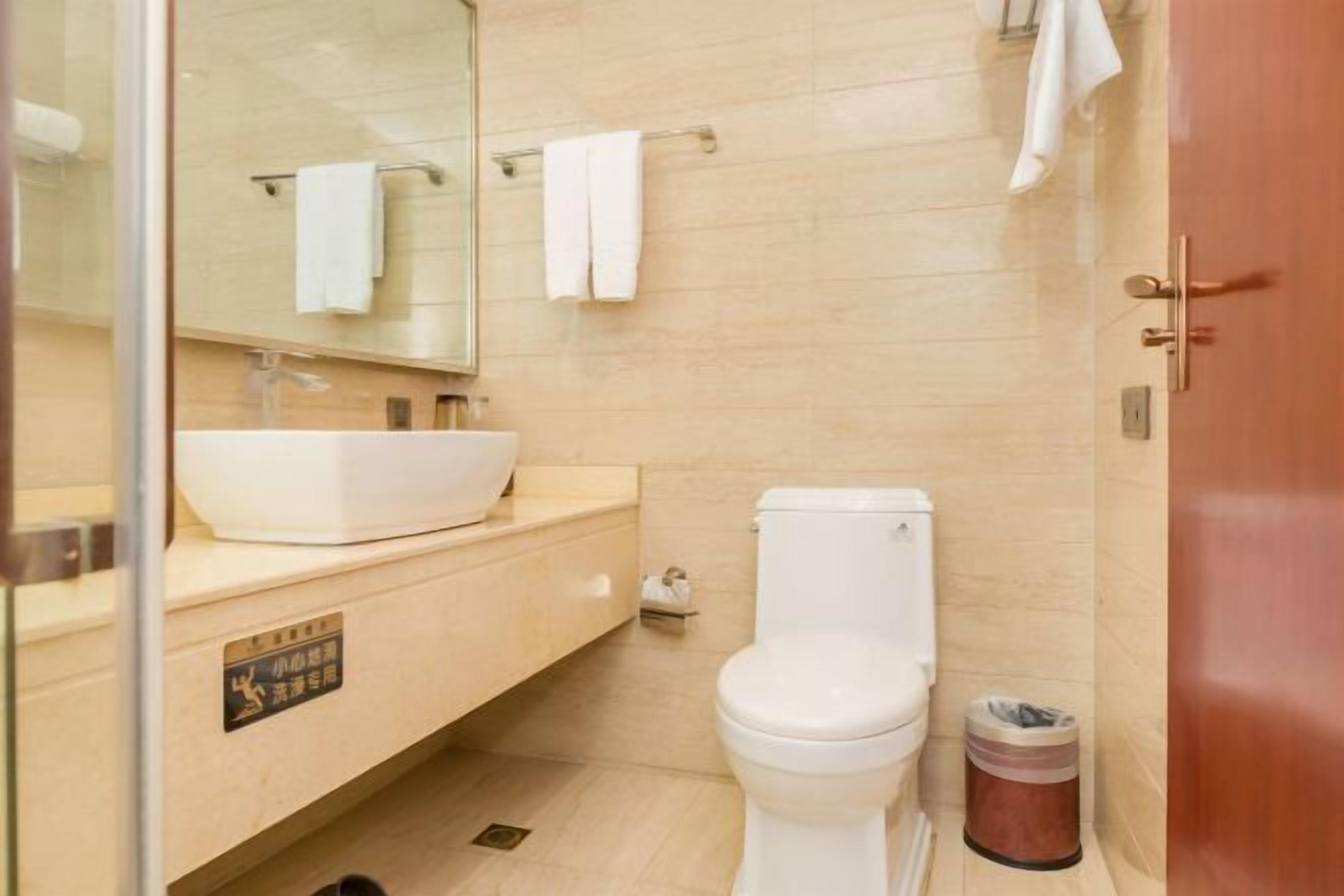 A bathroom with a white sink, toilet, and a trash bin.