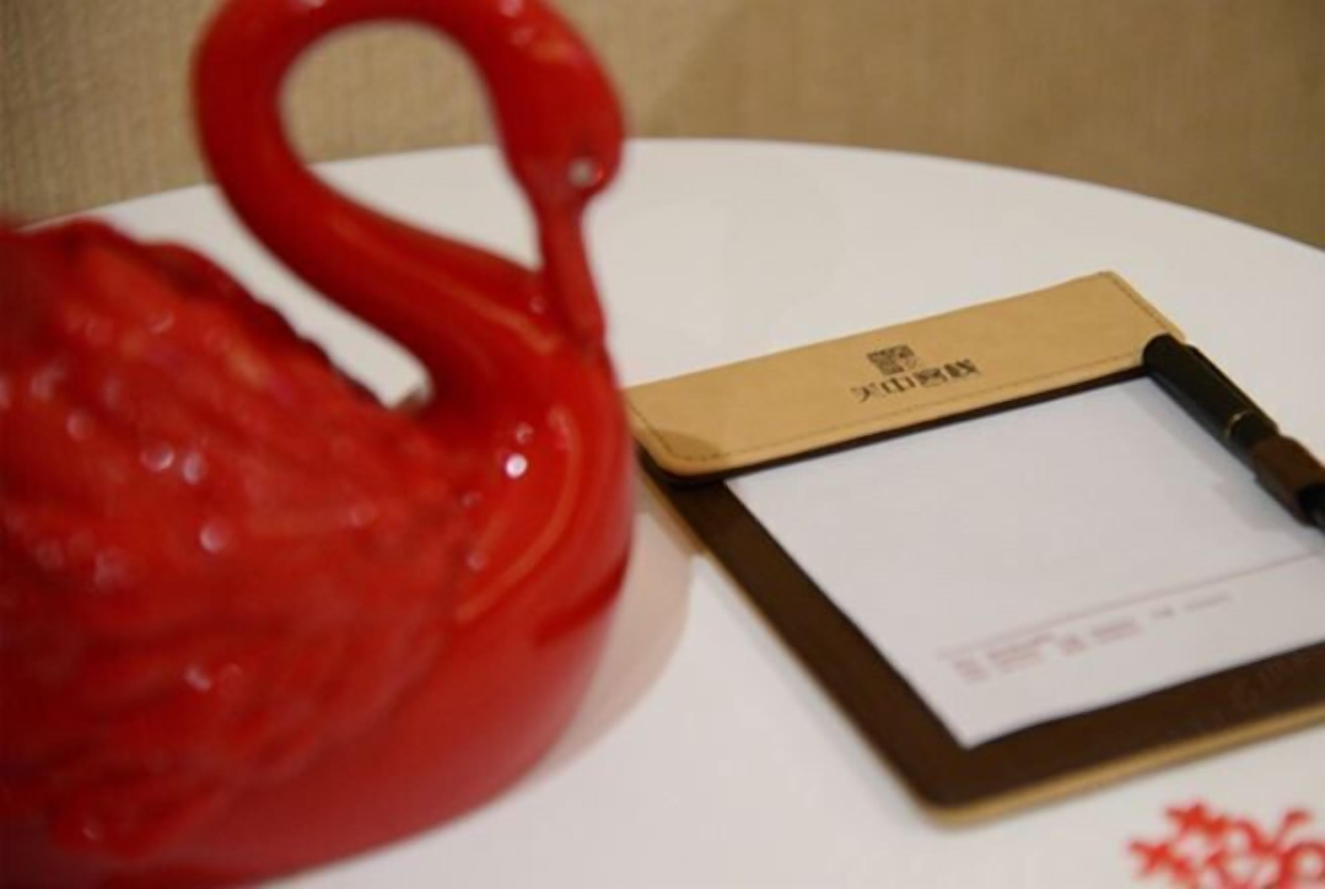 A red teapot on a white table with a brown notebook and pen beside it.