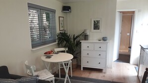 A compact living space with a dining table, a sofa, a white cabinet, and a potted plant. - Tranquil Wood Cabin set in a Beautiful Orchard (Penzance)
