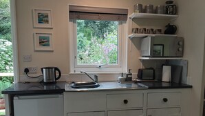 A small kitchenette with a window, a kettle, a microwave, and a sink. - Tranquil Wood Cabin set in a Beautiful Orchard (Penzance)