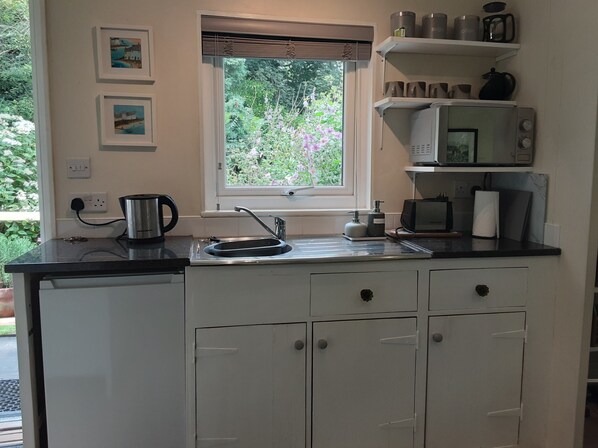 A small kitchenette with a window, a kettle, a microwave, and a sink.