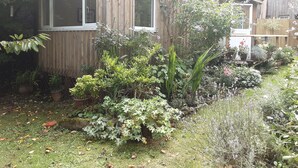 A wooden cabin with a garden in front, surrounded by various plants and flowers. - Tranquil Wood Cabin set in a Beautiful Orchard (Penzance)
