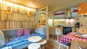 A cozy cabin interior with a wooden sofa, two round tables, and a kitchen area.