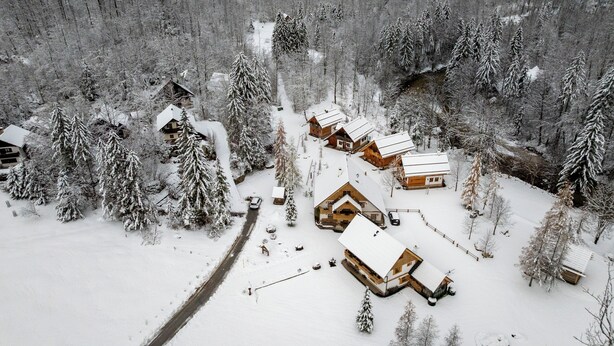 A snow-covered village with wooden cabins, a narrow road, and dense forest.