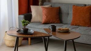 Un soggiorno moderno con un divano grigio, due tavolini in legno, una piccola pianta in vaso, una tazza e un piattino di biscotti.
