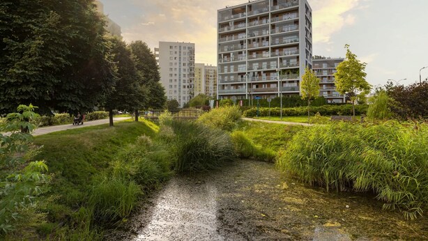 Un moderno edificio residenziale con numerosi balconi e un curato giardino dotato di un piccolo ruscello.