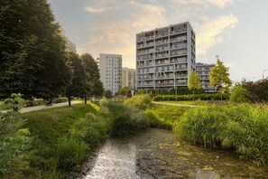 A modern apartment building with multiple balconies and a well-maintained garden area with a small stream.