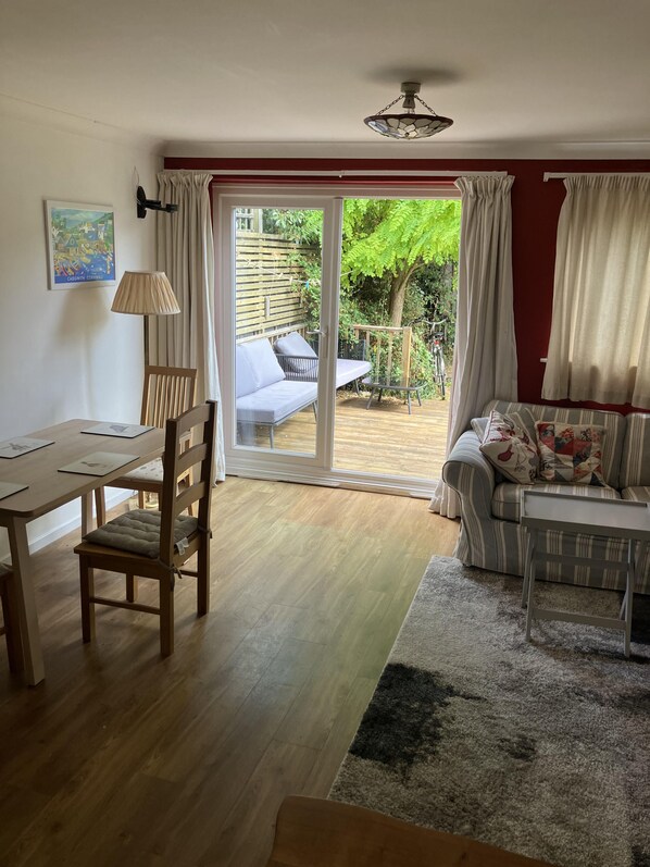 Relax in this open-plan living space with a dining area and seating area, featuring a sliding glass door leading to a garden with lush greenery and a bicycle view.