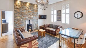 A modern living room with a stone wall, leather sofas, a glass dining table, and a fireplace. - Host & Stay | Boutique Balcony (Whitby)