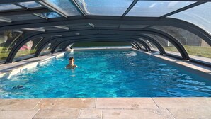 Una piscina amb una estructura de vidre i un paviment de rajola.