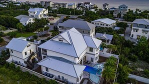 Une grande maison moderne dotée d’une piscine, entourée d’autres maisons et située à proximité d’une plage.