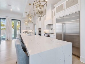 Une cuisine moderne dotée d’un grand îlot central, d’appareils électroménagers en acier inoxydable et de luminaires suspendus.