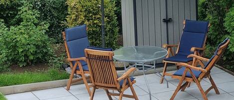 Eine Terrasse im Freien mit zwei Holzstühlen und einem Tisch, einem Sonnenschirm und einem Haus im Hintergrund.