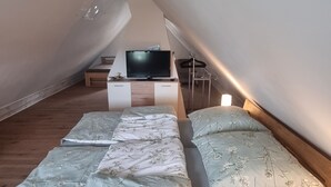 Ein Schlafzimmer mit schrägem Dach, einem Bett mit floralem Bettzeug, einem Fernseher auf einem Schrank und einem Holzboden.