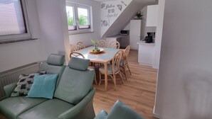 Ein modernes Wohnzimmer mit einem grünen Sofa, einem Esstisch mit Stühlen und einer Küche im Hintergrund.