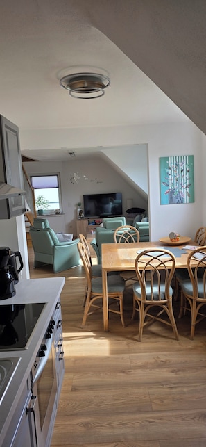 A modern kitchen with a stove, dining table, and chairs, a living area with a TV and seating, and a painting on the wall.
