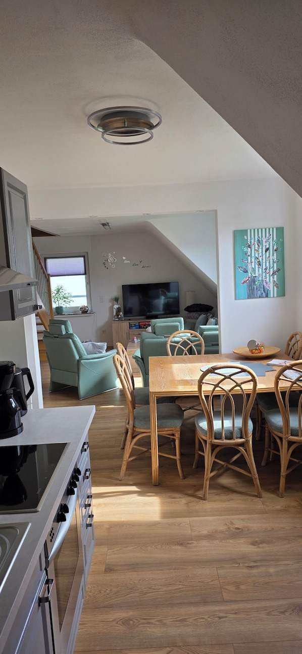 A modern kitchen with a stove, dining table, and chairs, a living area with a TV and seating, and a painting on the wall. - Ferienwohnung bis 7 Personen Sehr Zentral Gelegen (Brilon)