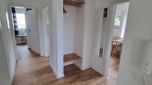 Ein geräumiger Flur mit Holzboden, weißen Wänden und einem Deckenventilator. Es führen Türen zu verschiedenen Räumen, und ein kleines Holzregal ist sichtbar.